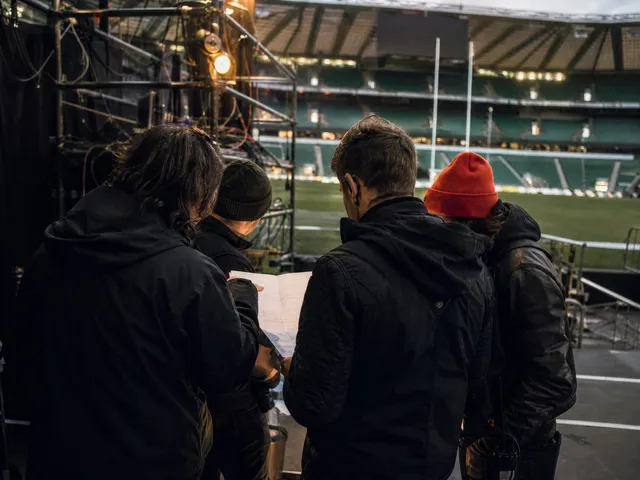 A sports event-production crew reviewing plans at the edge of a stadium before doors open
